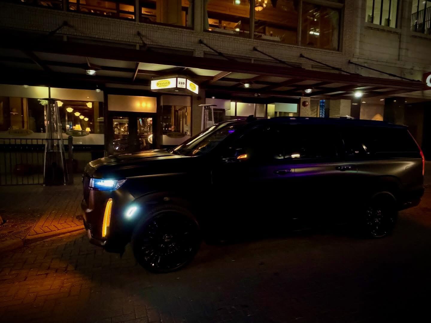 Luxury black SUV driving through Manhattan skyline at night with city lights reflecting on vehicle