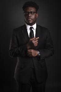 Stylish African American man in a black suit, looking confident and professional against a dark background.